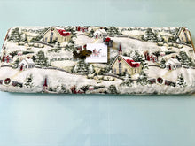 Load image into Gallery viewer, Bolt of Susan Wi get Country Church Christmas fabric featuring a winter village scene with snow-covered houses, trees, sheep, fences, garland, wreaths displayed on a light blue cutting mat.