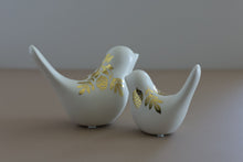 Load image into Gallery viewer, Two white ceramic bird figurines with gold leaf floral patterns, displayed on a neutral beige surface against a gray background.