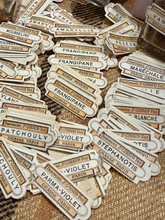 Load image into Gallery viewer, A pile of vintage-style perfume label stickers featuring names like Frangipane, Maréchale, and Patchouli, printed in beige and brown on a textured burlap background.