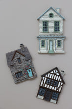 Load image into Gallery viewer, Three miniature decorative house figurines or magnets arranged on a plain light gray background: one gray stone house with a blue door, one white house with pale green trim, and one black-and-white timber-framed house.