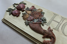 Load image into Gallery viewer, A close-up of a carved wooden decorative plaque featuring pomegranates, flowers, and a basket motif, with part of a large letter 'H' visible on the right side.