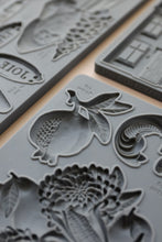 Load image into Gallery viewer, Gray silicone mold trays with embossed floral, fruit, and scroll designs, shown in a close-up angled view.