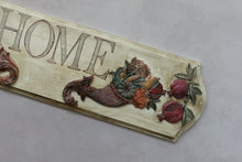 Load image into Gallery viewer, A decorative wooden sign with the word "HOME" in raised letters, featuring a carved cornucopia filled with fruits and vegetables, plus two pomegranates, on a light gray background.