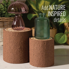 Load image into Gallery viewer, Two rustic brown textured cylindrical planters or vases displayed on a white surface with green plants in the background. One planter holds a ribbed translucent pink glass vase, and the other holds a ribbed translucent green glass bottle.