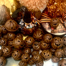 Load image into Gallery viewer, A collection of carved jack-o'-lantern metal bells in a warm rusty brown tone, arranged with Halloween-themed decorative props including a decorated pumpkin, orange-and-black striped ribbon, and a paper mache Halloween box in the background.