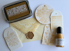 Load image into Gallery viewer, Iron Orchid Designs stamping kit featuring a gold ink pad, cream envelopes, decorative paper stamps, a wax seal, and a small bottle of ink on a white background.