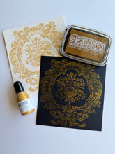 Load image into Gallery viewer, Iron Orchid Designs stamp ink set featuring a black stamp pad with gold foil ornamental pattern, a gold ink pad in a silver case, and a small bottle of gold ink on a white background.