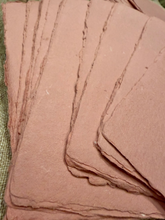 Load image into Gallery viewer, A close-up of several overlapping rectangular sheets of handmade paper with rough, uneven edges, fanned out on a textured green surface.