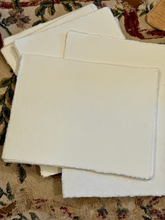 Load image into Gallery viewer, A stack of off-white handmade paper sheets with rough, unbleached edges, displayed on a patterned fabric surface.