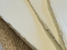Load image into Gallery viewer, Close-up of cream-colored textured fabric or wallpaper with irregular torn edges, shown overlapping a woven beige rug.
