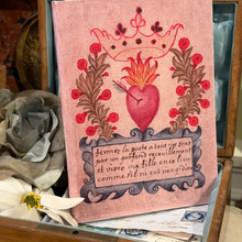 Load image into Gallery viewer, A pink decorative book or journal cover featuring a red Sacred Heart illustration with a crown, red berries, brown floral garlands, and a French inscription on a scroll, displayed among fabric flowers and papers.