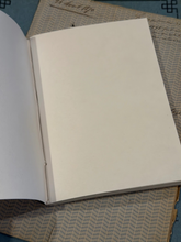 Load image into Gallery viewer, An open blank notebook or journal with blank white pages, resting on a patterned beige and gray fabric surface.