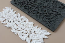 Load image into Gallery viewer, White 3D-printed leaf and berry floral trim shown next to a dark gray silicone mold that creates the same leaf pattern, on a solid beige background.