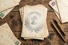 Load image into Gallery viewer, A stack of vintage aged paper letters with a central illustration of an angel, displayed on a rustic wooden table alongside old stamps and two fountain pens.