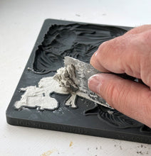 Load image into Gallery viewer, A close-up of a hand applying gray modeling compound to a black rubber or silicone mold cavity, with the embossed design reading 'JOD SILENTNIGHT' visible on the mold edge.