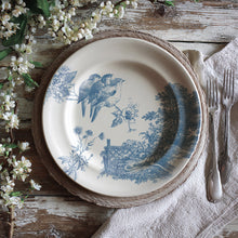 Load image into Gallery viewer, Decorative plate stamped with IOD Meadowlark Decor Stamp featuring a blue bird and landscape design on a rustic wooden table with flowers and cutlery.