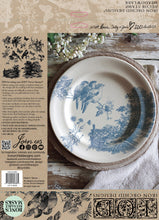 Load image into Gallery viewer, View of back of IOD Meadowlark Decor Stamp packaging depicting a pretty plate with a stamped blue bird and landscape design in a rustic table setting.