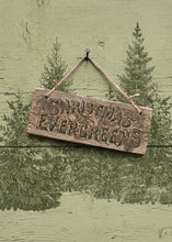 Load image into Gallery viewer, A rustic wooden hanging sign with the words “Christmas Evergreens” carved into the front, suspended by twine from a peg against a distressed sage green wall with painted evergreen trees.
