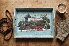 Load image into Gallery viewer, A rustic distressed light blue wooden serving tray with a hand-painted winter cabin scene, styled on a wooden table with a brown leather strap, a cup of coffee, and a knit glove.