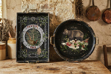 Load image into Gallery viewer, A rustic decorative serving tray set displayed on a wooden table against a stone wall. The set includes a rectangular black tray with ornate green vine borders and a central circular illustration, and a round black tray with brass handles, both featuring a painted bear and floral design.