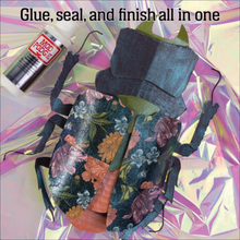 Load image into Gallery viewer, A beetle-shaped craft item made from patterned fabric and dark material, shown with a bottle of Mod Podge glue on a shiny iridescent background. Text at the top reads, 'Glue, seal, and finish all in one.