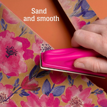 Load image into Gallery viewer, A close-up shows a hand using a bright pink handheld sanding block to smooth floral-patterned paper over an orange surface. White text reads 'Sand and smooth.
