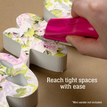 Load image into Gallery viewer, A hand uses a bright pink sander to sand a floral-patterned wooden decorative piece on a brown background, with the text 'Reach tight spaces with ease' and '*Mini sander not included'.