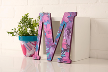 Load image into Gallery viewer, Decorative letter 'M' decoupage project with floral pattern on a white surface next to a plant created with Mod Podge Satin Glue and Sealer.
