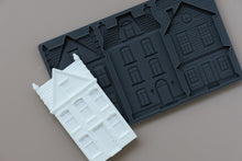 Load image into Gallery viewer, A dark gray silicone mold with embossed house-shaped cavities, shown with a white molded house sample piece on a plain taupe background.