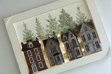 Load image into Gallery viewer, A framed miniature art piece depicting four detailed vintage houses in warm brown, gray, and red tones, set against a background of green pine trees, all enclosed in a white textured frame.