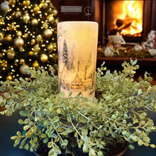 Load image into Gallery viewer, Decorative candle with a winter scene design in front of a Christmas tree and fireplace.