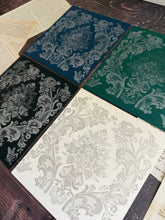 Load image into Gallery viewer, Four square fabric or paper swatches with ornate damask floral patterns in blue, green, black, and off-white, arranged on a dark wood surface with vintage book pages.