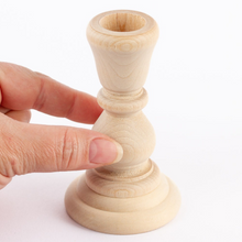 Load image into Gallery viewer, A hand holding a small unfinished wooden candlestick holder against a plain white background.