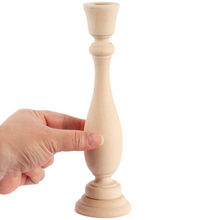 Load image into Gallery viewer, A hand holding a small unfinished wooden candlestick holder against a plain white background.