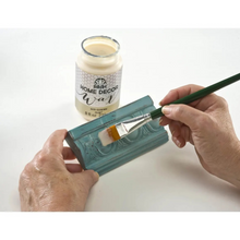Load image into Gallery viewer, Hands applying a teal decorative wax finish to a rectangular block with a paintbrush, with a jar of Scentsy Home Decor Wax in the background on a white surface.