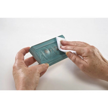 Load image into Gallery viewer, A pair of hands holding a teal rectangular decorative block or tile while wiping it with a white cloth on a plain white background.