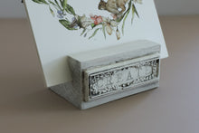 Load image into Gallery viewer, A small rectangular white and gray decorative stand with the word CREATE embossed on the front, holding a printed card with a floral illustration, on a beige surface.